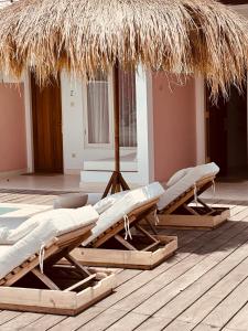 two lounge chairs under a straw umbrella on a deck at Motel LOVE SONG Canggu in Canggu