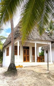 a white house with a thatched roof and a palm tree at Jumamosi Beach Villa in Ushongo Mabaoni