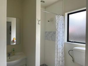uma casa de banho branca com um chuveiro e um lavatório. em Summer Inn Motel em Orewa
