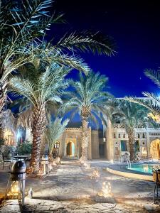 a courtyard with palm trees and a pool at night at Hotel ksar merzouga in Merzouga