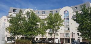 ein großes weißes Gebäude mit Bäumen davor in der Unterkunft Les jardins du Carrousel - Chambre privée aménagée en T2 in Noisy-le-Grand