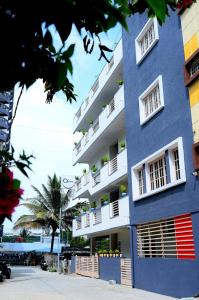 バンガロールにあるUrban Stay Adams Service Apartmentの白い窓とヤシの木のある青い建物