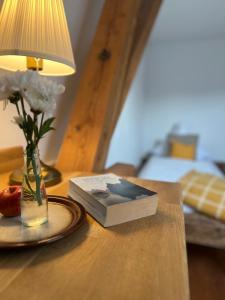 a book on a table with a vase of flowers and a lamp at Seeberghof in Frasdorf