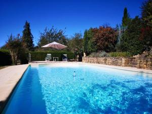 a blue swimming pool with a table and an umbrella at Maison en pierre avec piscine in Lavergne