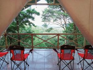 a porch with red chairs and a view of trees at Volcano Tenorio Glamping Ranch - 3 Tents in Rio Celeste