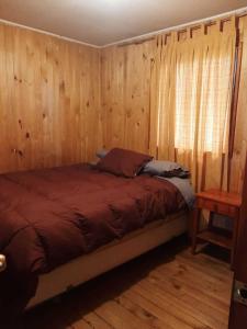 Un dormitorio con una cama con paredes de madera y una ventana en Cabaña Agradable, en Pucón