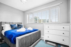 a bedroom with a bed with blue sheets and a dresser at 3 Bed Family House in Solihull ☆ LARGE GARDEN & FREE PARKING ✪ BY (BHX) Birmingham Airport → (NEC) National Exhibition Centre, Resorts World Birmingham, Jaguar Land Rover Solihull - BY PILOT MY PROPERTY ® in Water Orton