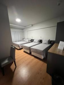 two beds in a room with a desk and a chair at Hoteis Cattoni in Lages