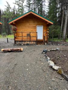 una cabaña de madera con una puerta blanca en el bosque en Carlo Creek Cabins en McKinley Park