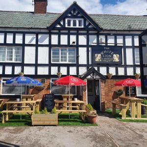 un antiguo edificio en blanco y negro con mesas y sombrillas en The White Lion Inn, en Brinklow