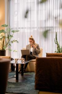 Eine Frau auf einer Couch mit einem Laptop und einem Telefon in der Unterkunft Quality Hotel Carlia in Uddevalla