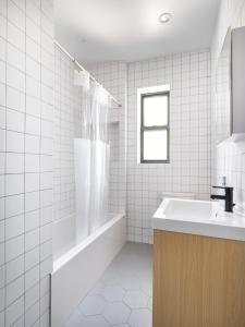 Baño de azulejos blancos con lavabo y bañera en Modern Three Bedroom Brooklyn Condo-Hotel, en Brooklyn