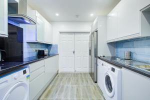 cocina con armarios blancos, lavadora y secadora en Charming 7 bedroom house sleeps up to 13 guests en Romford