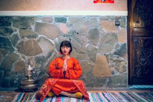 Una donna seduta sul pavimento di fronte a un muro di pietra di Riad Chay & Boutique a Ouarzazate