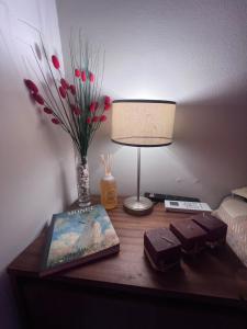 un escritorio con una lámpara y un libro y un jarrón con flores en Departamento céntrico y tranquilo en Villa Marini