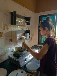 Uma mulher a mexer uma tigela de comida na cozinha. em Hostel Osara em Bodh Gaya