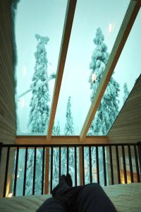 a person laying on a bed looking out of a window at Villa Auroras Karhu in Syöte