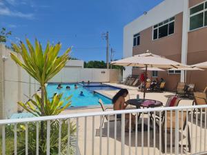 a woman sitting at a table next to a swimming pool at Ap Grão de Areia - Praia dos Milionários Ilhéus-BA in Ilhéus
