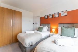 a bedroom with two beds and an orange wall at Stylish House - Close to City Centre - Free Parking, Super-Fast Wifi and Smart TVs by Yoko Property in Coventry