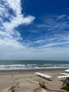 una playa con varias sombrillas blancas y el océano en 5 Soles II en Pinamar