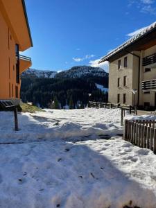 a snow covered ground next to a building with a mountain at LUW casa a Madonna di Campiglio in Madonna di Campiglio
