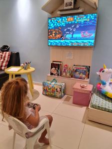 a little girl sitting in a chair watching a tv at Tabatinga Residence Flat Family Kids 04 in Conde