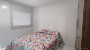 a white bedroom with a bed with a colorful comforter at Casa mobiliada de 2 suítes na R São Lázaro 2367 - 2370 - Jardim Gonzaga in Juazeiro do Norte