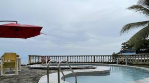 uma piscina com um guarda-sol vermelho e uma mesa e cadeiras em Hotel les Polygones Kribi em Kribi