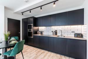 a kitchen with black cabinets and a table with green chairs at Modern Sky-High Flat In North Acton in London
