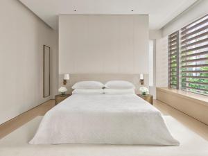 a white bedroom with a large bed with white sheets at The Singapore EDITION in Singapore