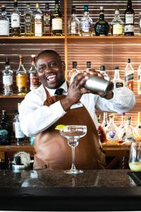 un homme debout derrière un bar préparant un verre dans l'établissement The Bay Hotel, au Cap