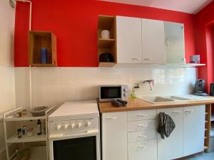 une cuisine avec des placards blancs et un mur rouge dans l'établissement Grand T2 très fonctionnel à deux pas du centre - Morel Ladeuil, à Clermont-Ferrand