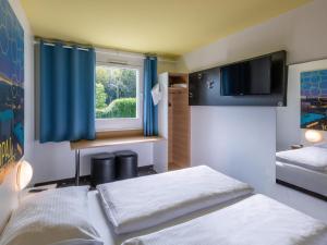 een slaapkamer met 2 bedden en een raam met blauwe gordijnen bij B&B HOTEL Aachen-Würselen in Würselen