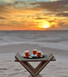 a tray with three drinks on a table with the sunset at Luxury Camp Dunes Insolites Sabria in Sabria