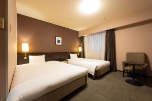 una camera d'albergo con due letti e una sedia di Smile Hotel Premium Kanazawa Higashiguchiekimae a Kanazawa