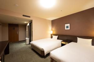 una camera d'albergo con due letti e uno specchio di Smile Hotel Premium Kanazawa Higashiguchiekimae a Kanazawa