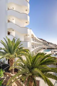 a white building with palm trees in front of it at Apartamentos Cabau Altair in Puerto Rico de Gran Canaria