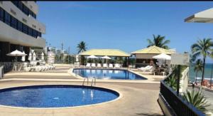 a large swimming pool next to a resort with the ocean at apart hotel 2 quartos frente mar in Salvador