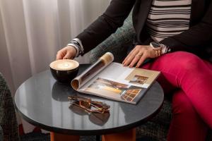 a woman sitting at a table with a cup of coffee and a book at Rydges Auckland in Auckland