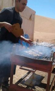 un hombre cocinando comida en una parrilla en el desierto en Bivouac Erg chegaga, en Zagora