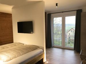 1 dormitorio con cama, TV y balcón en FourElements Grand Chalet, en Blankenburg