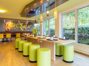 a bar with yellow stools in a restaurant with windows at B&B HOTEL Dortmund-Messe in Dortmund