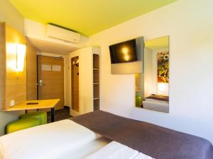Cette chambre comprend un lit, un bureau et une télévision. dans l'établissement B&B HOTEL Dortmund-Messe, à Dortmund