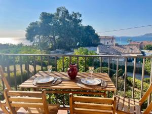una mesa de madera con vasos y platos en el balcón en Appartement cosy vue mer à 50 m de la plage - refait à neuf et climatisé, en Le Pradet