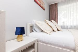 Dormitorio blanco con cama blanca y lámpara azul en Pušyno Apartment 1, en Klaipėda