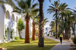 a woman walking down a sidewalk next to palm trees at Monarque Club Rivage - VV in Monastir