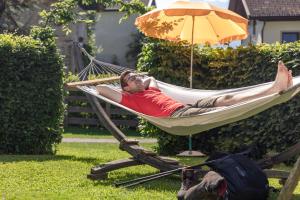 a man laying in a hammock under an umbrella at Apartmenthaus - Erlebenswert Bauernhof Gruber in Sankt Lorenzen im Lesachtal