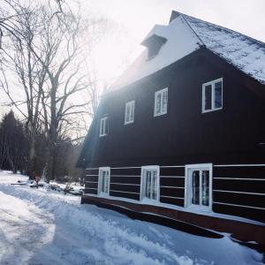 a black house with snow on the side of it at Roubenka U Andělů, Šumava in Kašperské Hory