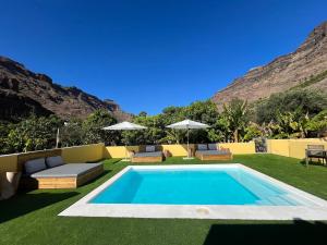 a swimming pool in the middle of a yard with grass and mountains at SUNNY CARMELITO DELUXE in Mogán