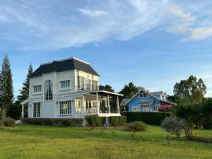 ein weißes Haus mit schwarzem Dach auf einem grünen Feld in der Unterkunft Misty English Cottage in Ban Non Na Yao